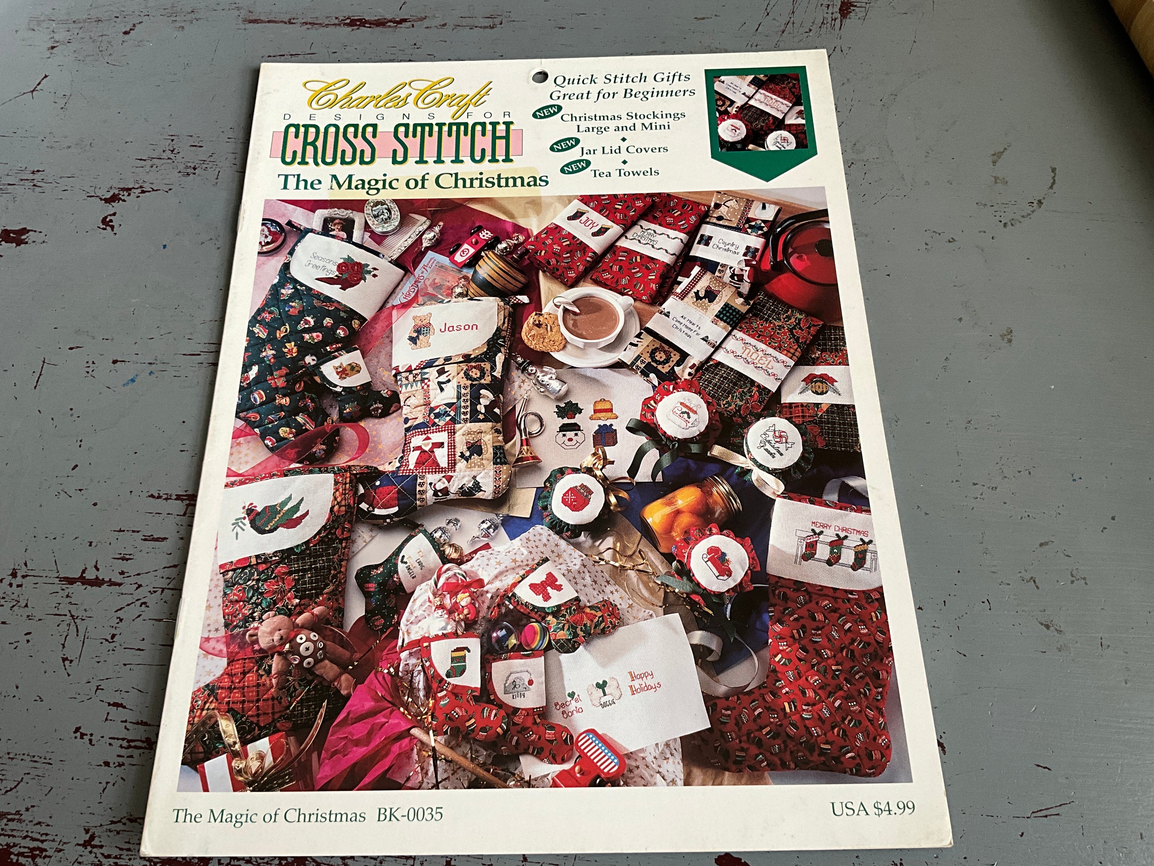 Cross stitch pattern book titled 'The Magic of Christmas' by Charles Craft on a gray surface.