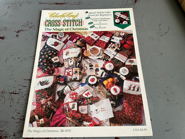 Cross stitch pattern book titled 'The Magic of Christmas' by Charles Craft on a gray surface.